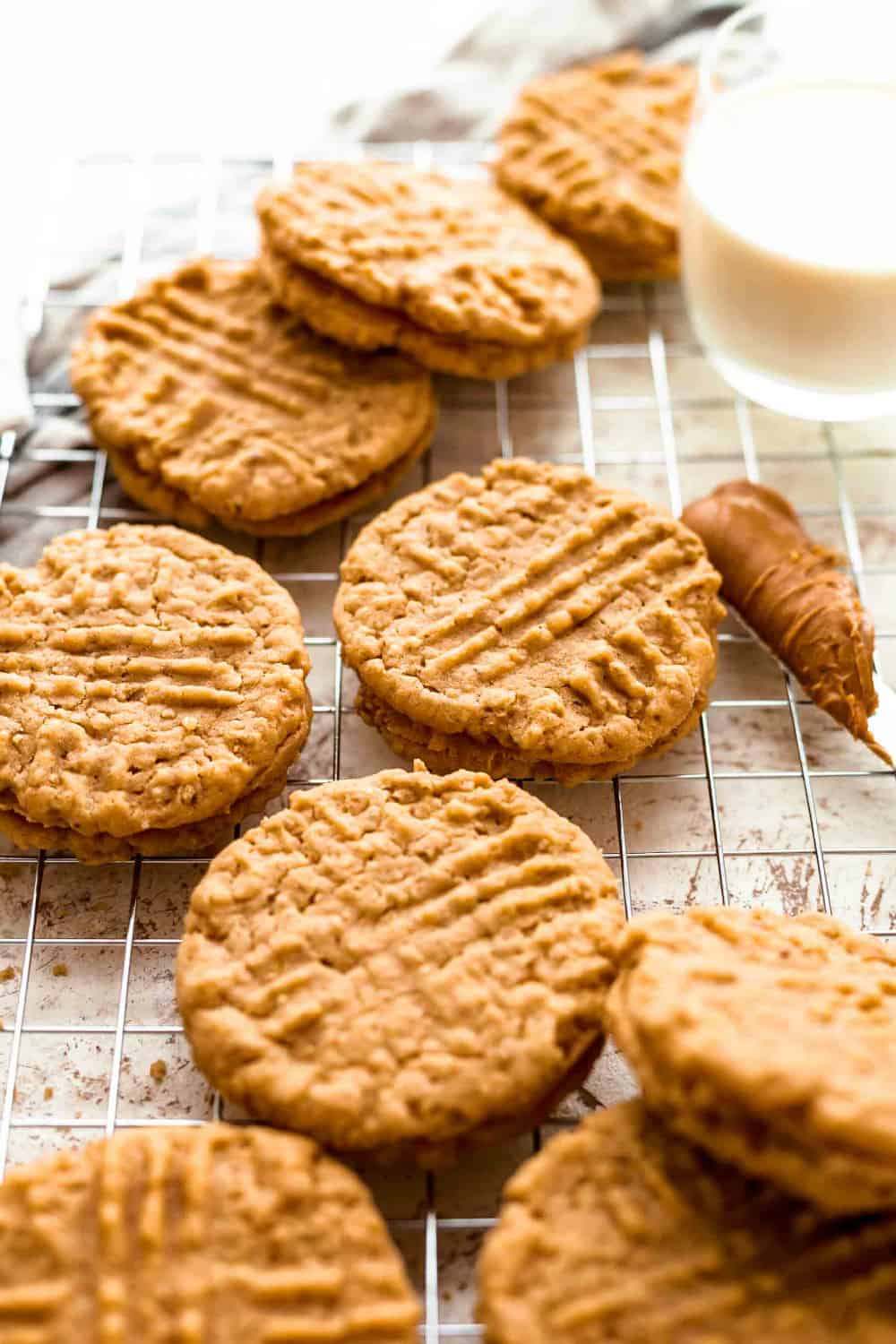 Assembled peanut butter sandwich cookies scattered on a baking rack next to a knife with peanut butter on it