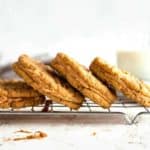 Peanut butter sandwich cookies stacked on a baking rack with a glass of milk in the background