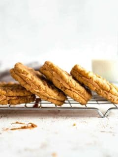 Peanut butter sandwich cookies stacked on a baking rack with a glass of milk in the background