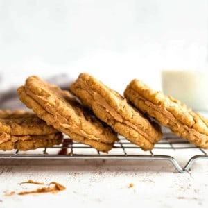 Peanut butter sandwich cookies stacked on a baking rack with a glass of milk in the background