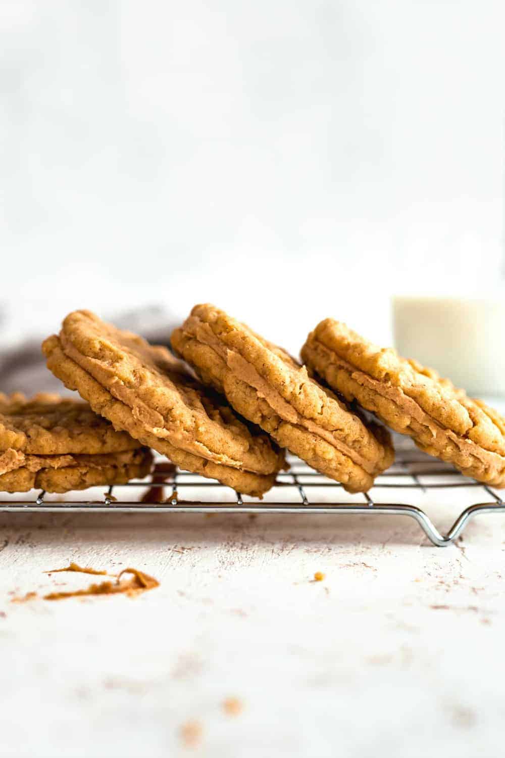 Peanut butter sandwich cookies stacked on a baking rack with a glass of milk in the background