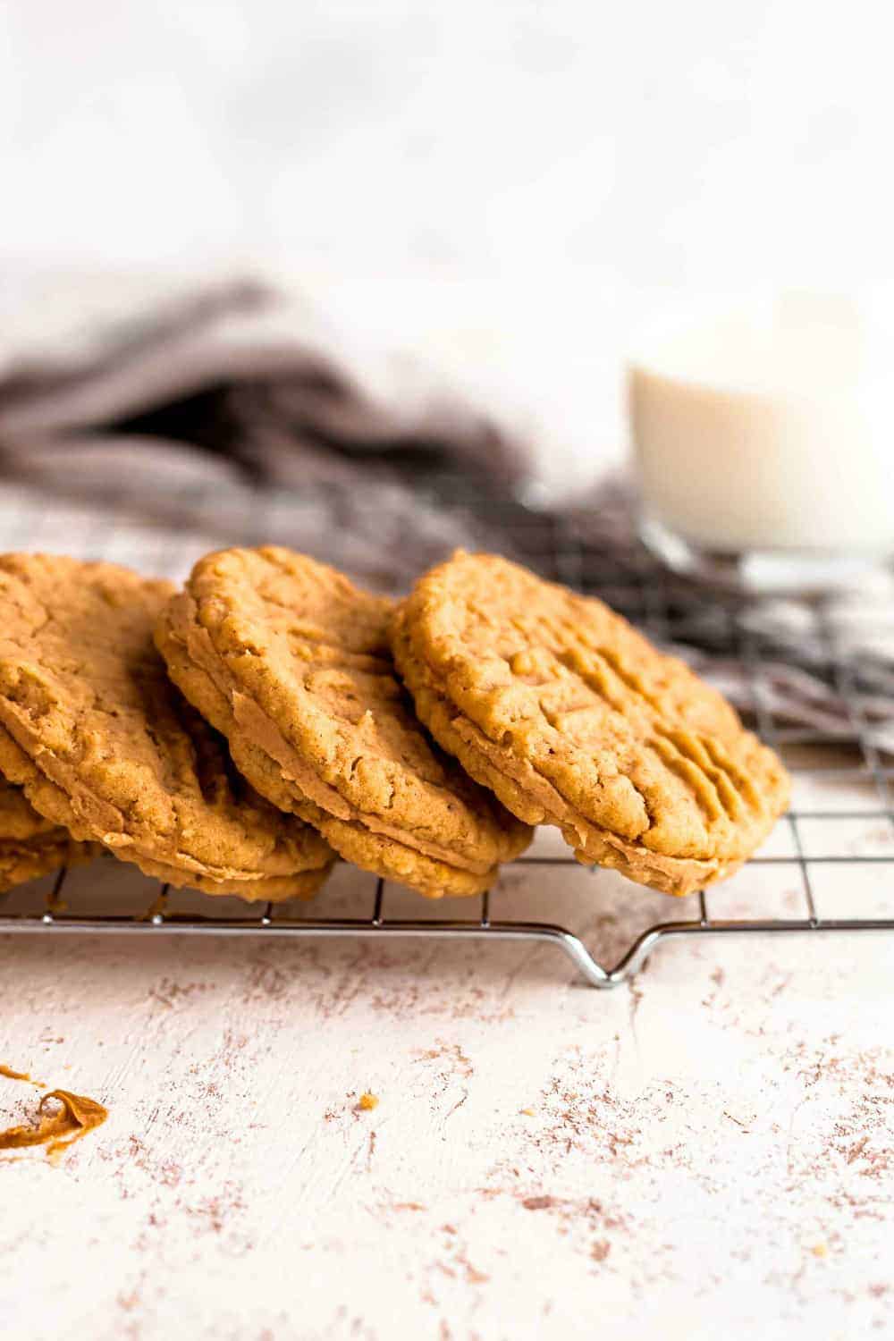 Side view of three peanut butter sandwich cookies stacked on a baking rack with dish towel in the background