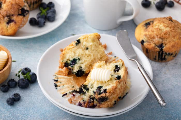 Halved blueberry crumb muffin topped with a pat of butter on a white plate.