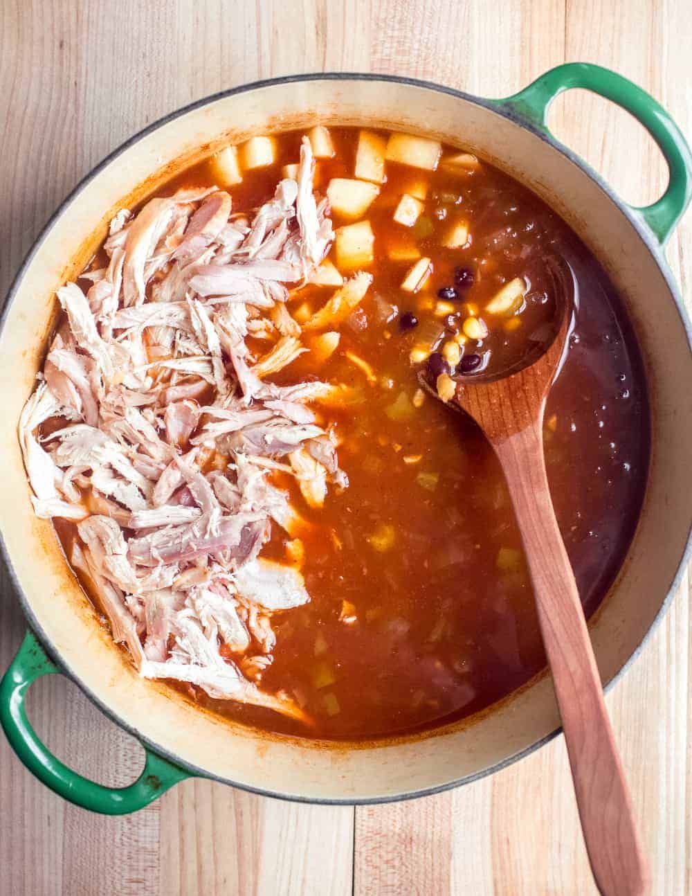 Shredded chicken being added to a pot of tortilla soup