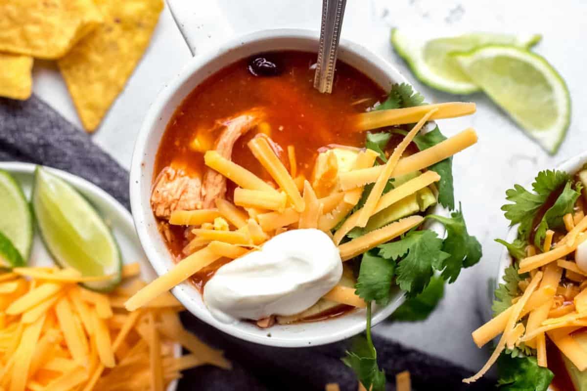 Spoon in a white mug of tortilla soup topped with cheese and sour cream