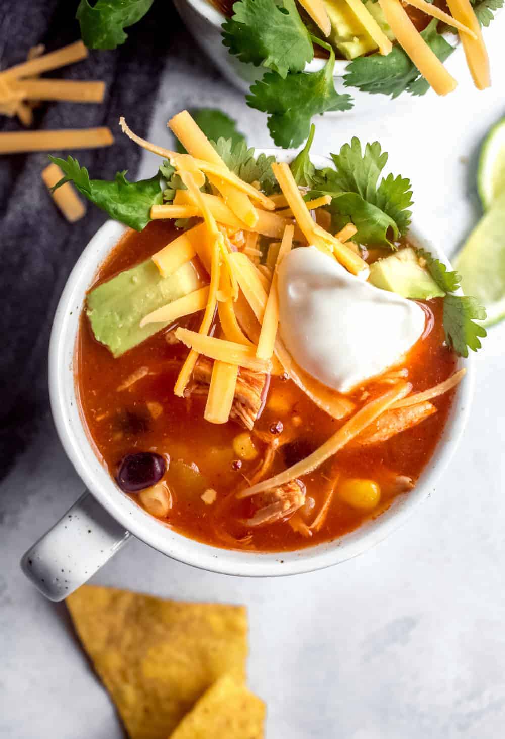 Close up view of a mug of tortilla soup topped with cheese, sour cream and avocado
