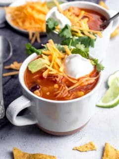 Tortilla soup in a white mug, topped with cheese and sour cream