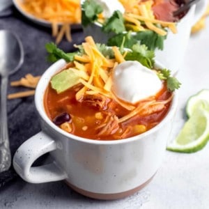 Tortilla soup in a white mug, topped with cheese and sour cream