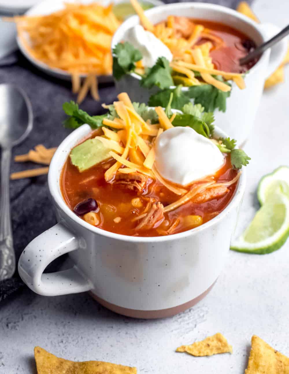 Tortilla soup in a white mug, topped with cheese and sour cream