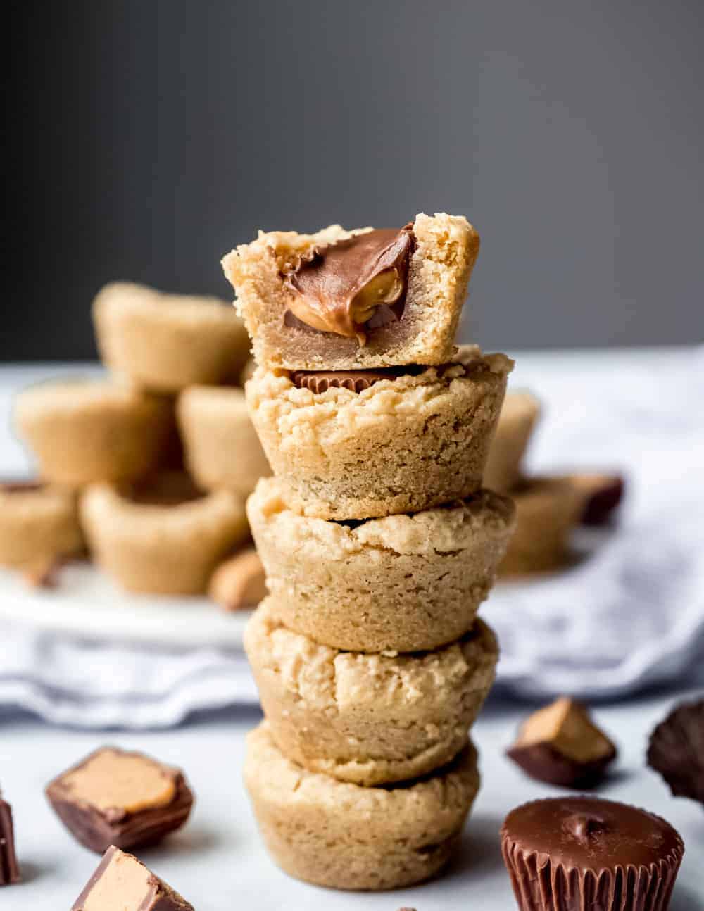 Close up of half of a peanut butter cup cookie showing the gooey peanut butter and chocolate center. The cookie is on top of a stack of peanut butter cup cookies