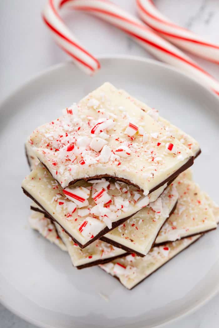Stack of peppermint bark pieces on a white plate. The top piece has a bite taken from the corner.