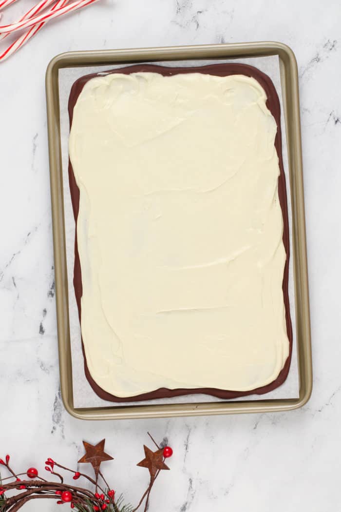 White chocolate spread on top of dark chocolate on a parchment-lined baking sheet.