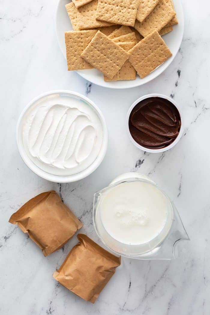 Overhead view of ingredients for eclair cake in bowls arranged on a marble counter