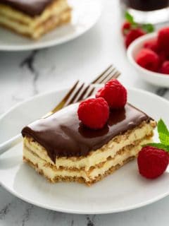 Fork next to a slice of eclair cake topped with fresh raspberries on a white plate