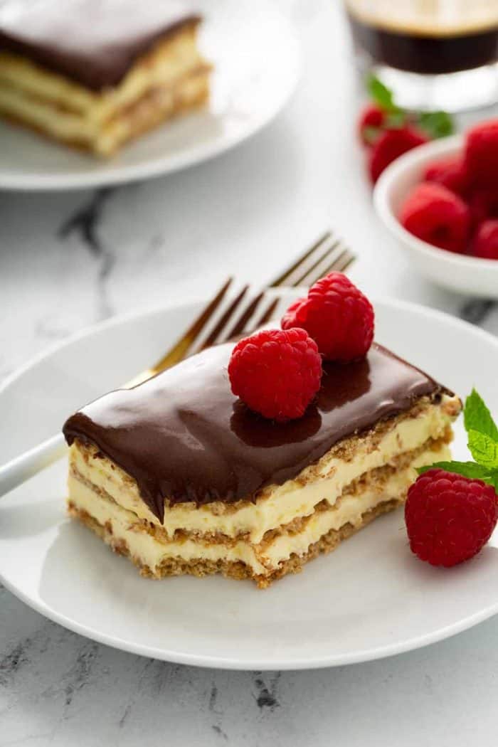 Fork next to a slice of eclair cake topped with fresh raspberries on a white plate