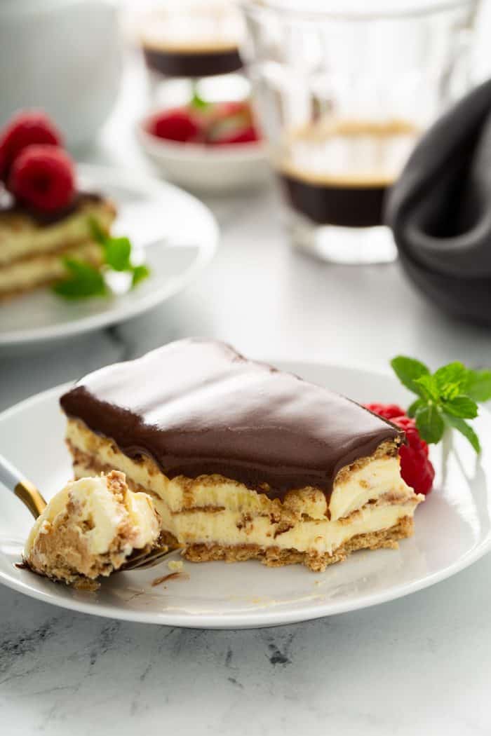 Fork holding a bite of eclair cake on a white plate next to a full slice of eclair cake