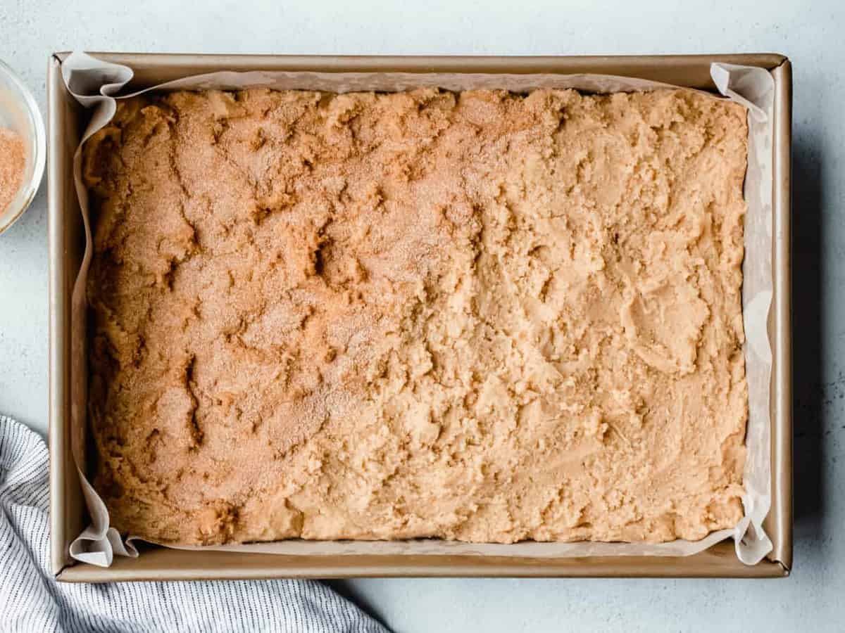 Dough for snickerdoodle blondies in a pan, with half of the dough covered with cinnamon-sugar