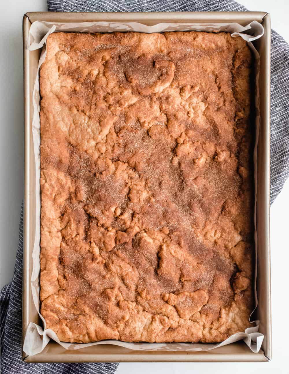 Freshly-baked snickerdoodle blondies in a parchment-lined pan, ready to be cut