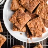 Cut snickerdoodle blondies arranged on a white plate that is set on a wire rack