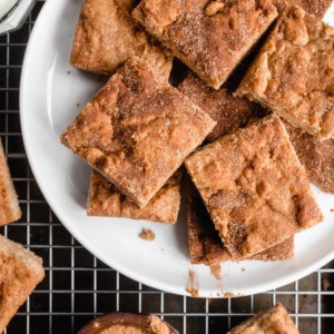 Cut snickerdoodle blondies arranged on a white plate that is set on a wire rack