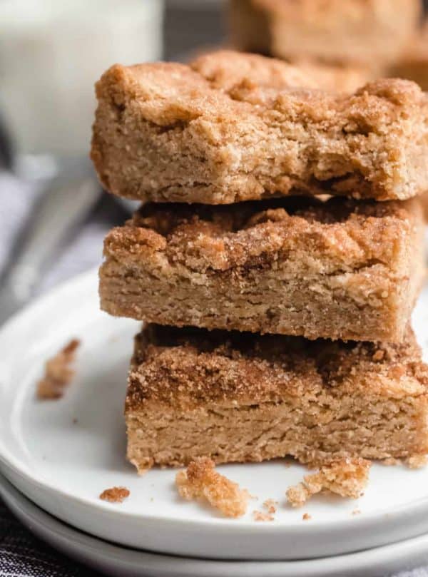 Three stacked snickerdoodle blondies on a white plate. The top blondie has a bite taken out of it.