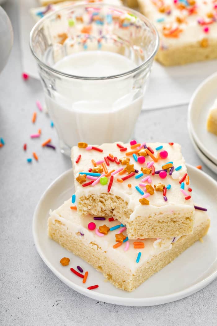 Two sugar cookie bars stacked on a white plate with a bite taken out of the corner of the top one