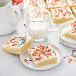 Sugar cookie bars topped with colorful sprinkles next to a glass of milk