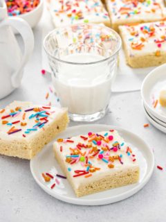 Sugar cookie bars topped with colorful sprinkles next to a glass of milk
