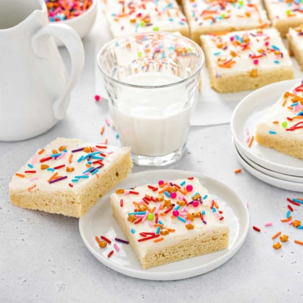 Sugar cookie bars topped with colorful sprinkles next to a glass of milk