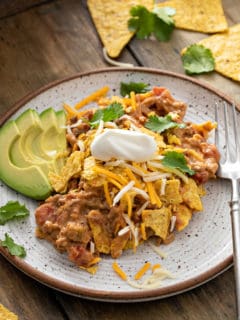 Taco casserole on a stoneware plate next to a fork and sliced avocado.