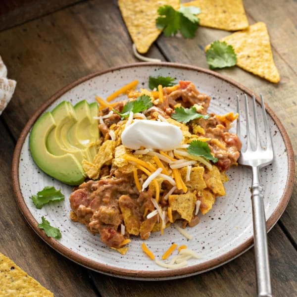 Taco casserole on a stoneware plate next to a fork and sliced avocado.