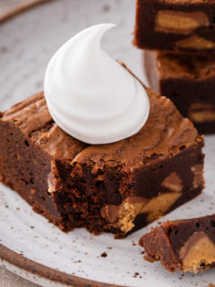 Peanut butter cup brownie topped with a dollop of whipped cream on a plate. A fork has taken a bite from the corner of the brownie.