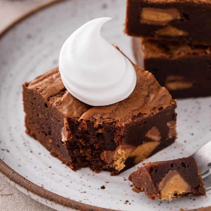 Peanut butter cup brownie topped with a dollop of whipped cream on a plate. A fork has taken a bite from the corner of the brownie.