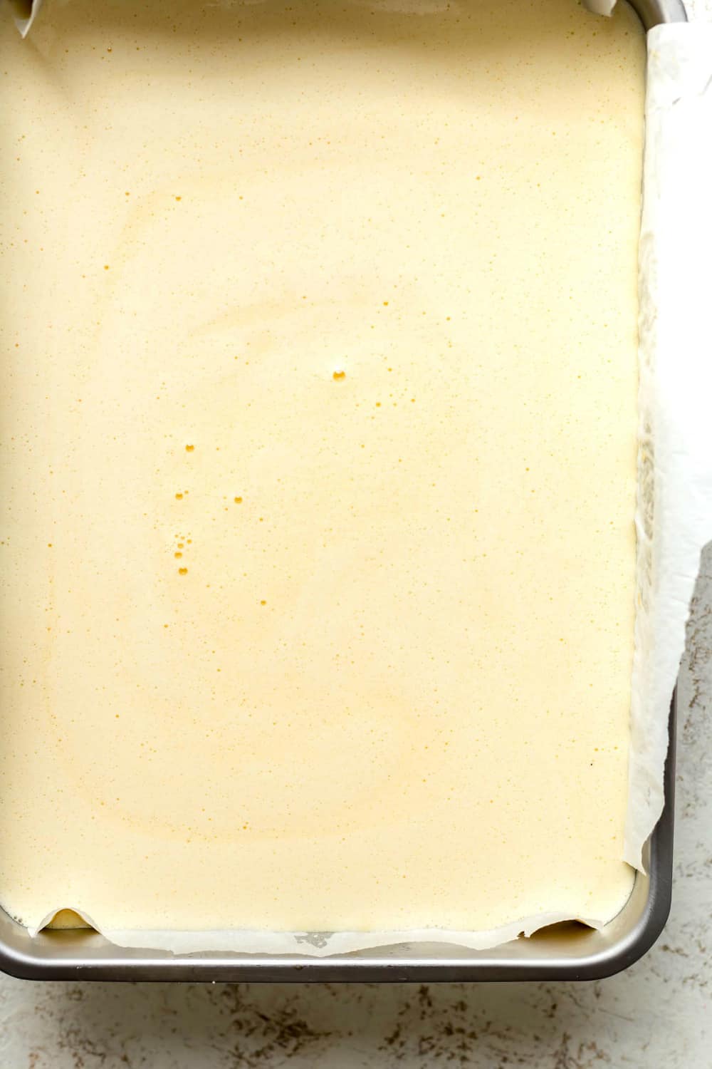 Overhead view of unbaked lemon bars in a parchment-lined metal pan