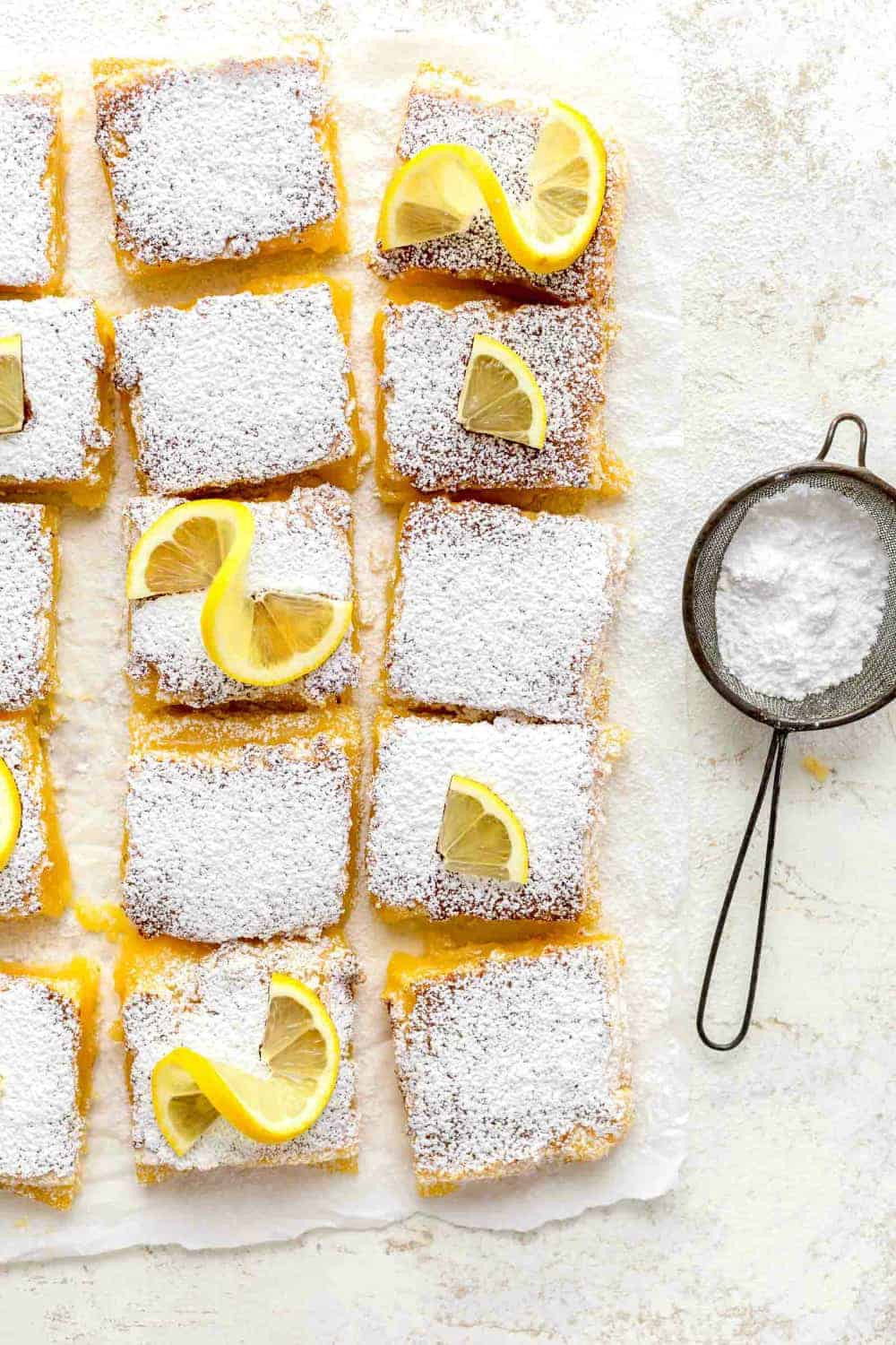 Overhead view of sliced homemade lemon bars next to a duster filled with powdered sugar