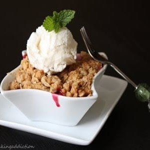 Cherry Crisp with a scoop of vanilla ice cream in a white, square bowl on a white square plate with a fork leaning on the right side of the bowl.