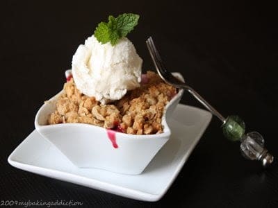 Cherry Crisp with a scoop of vanilla ice cream in a white, square bowl on a white square plate with a fork leaning on the right side of the bowl.