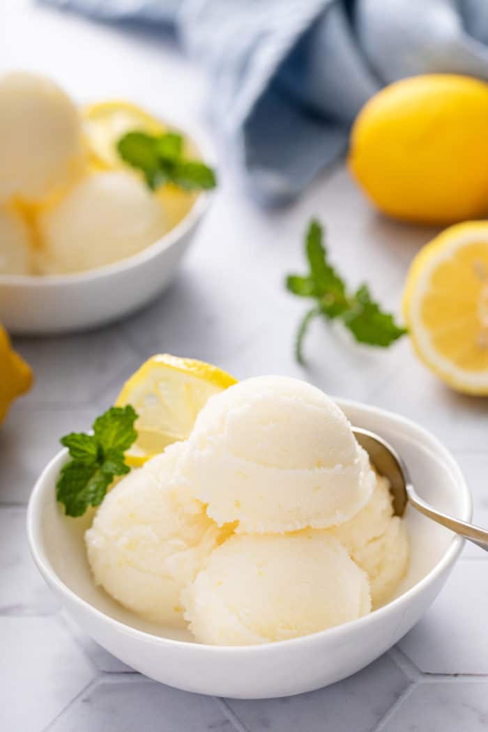 Spoon nestled into several scoops of lemon sorbet in a white bowl.