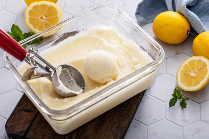 Glass dish filled with frozen lemon sorbet, with an ice cream scoop scooping out a portion of the sorbet.