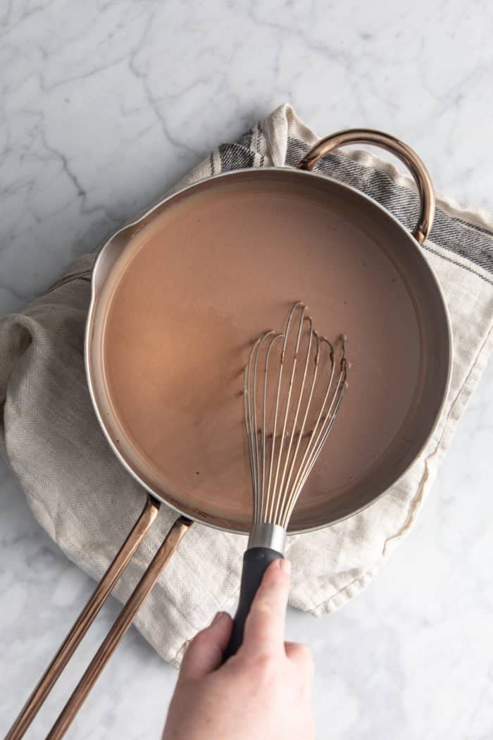 Chocolate ice cream base being whisked in a saucepan.