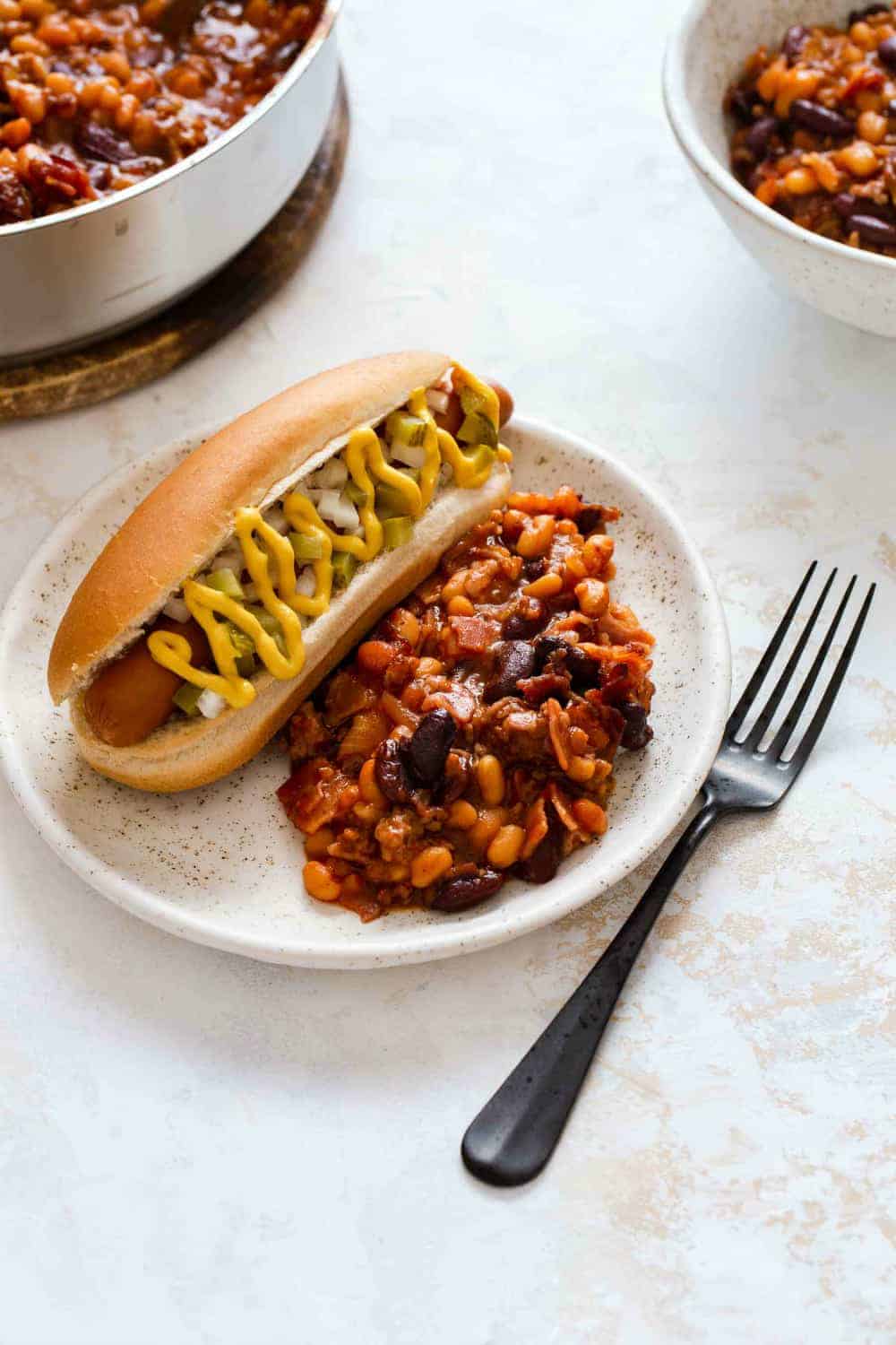 Old fashioned baked beans and a hot dog on a white plate