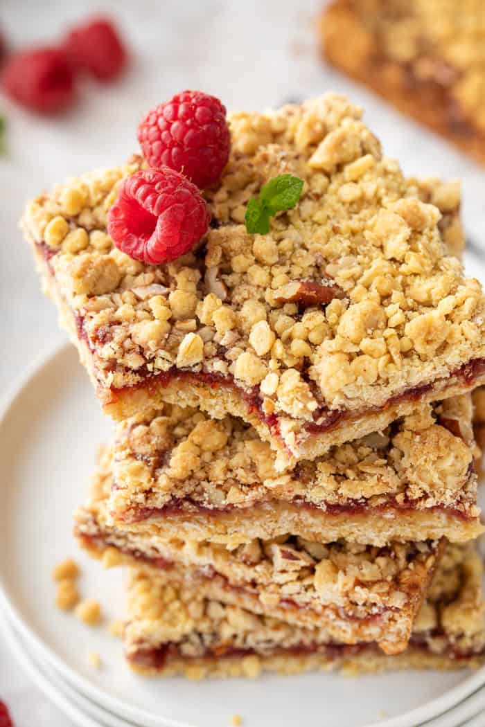 Raspberry bars stacked on a white plate, with a bite taken out of the corner of the top bar