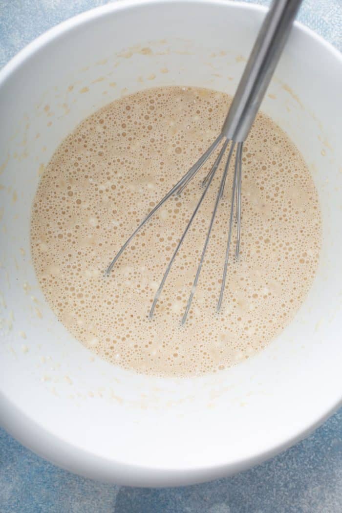 Whisk stirring banana pancake batter inside a white mixing bowl