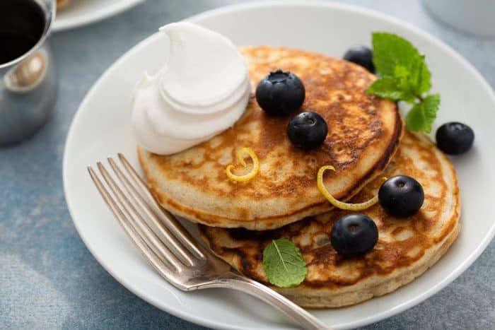 Fork and two banana pancakes, topped with blueberries and whipped cream, on a white plate