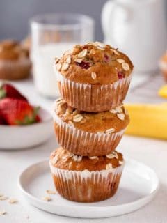 Three strawberry banana muffins stacked on a white plate.