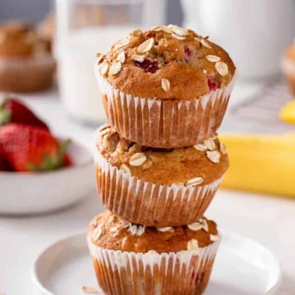 Three strawberry banana muffins stacked on a white plate.