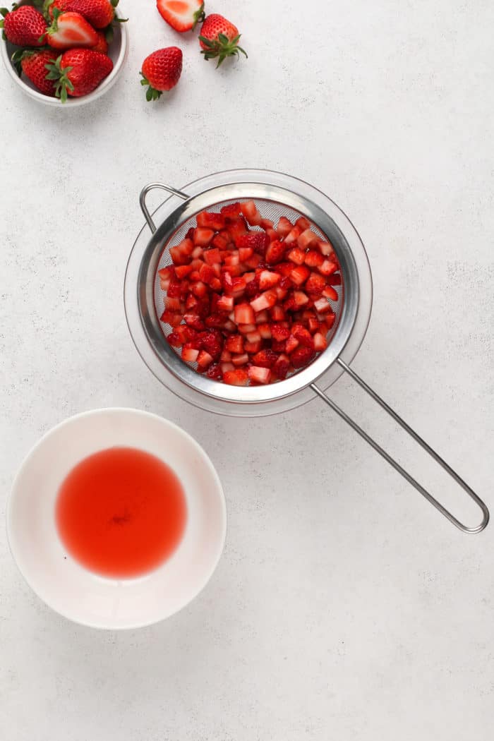Macerated strawberries in a strainer next to a bowl of the strawberry juice.