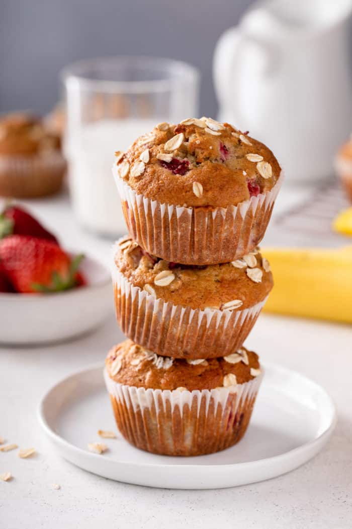 Three strawberry banana muffins stacked on a white plate.