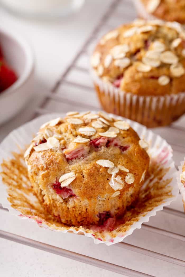 Unwrapped strawberry banana muffin set on a wire cooling rack with more muffins visible in the background.