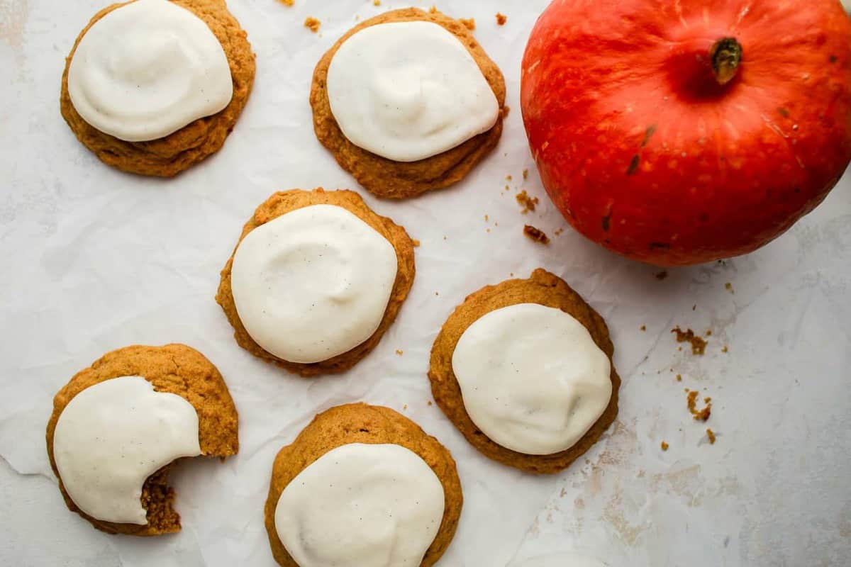 Pumpkin cookies topped with cream cheese icing next to a pumpkin